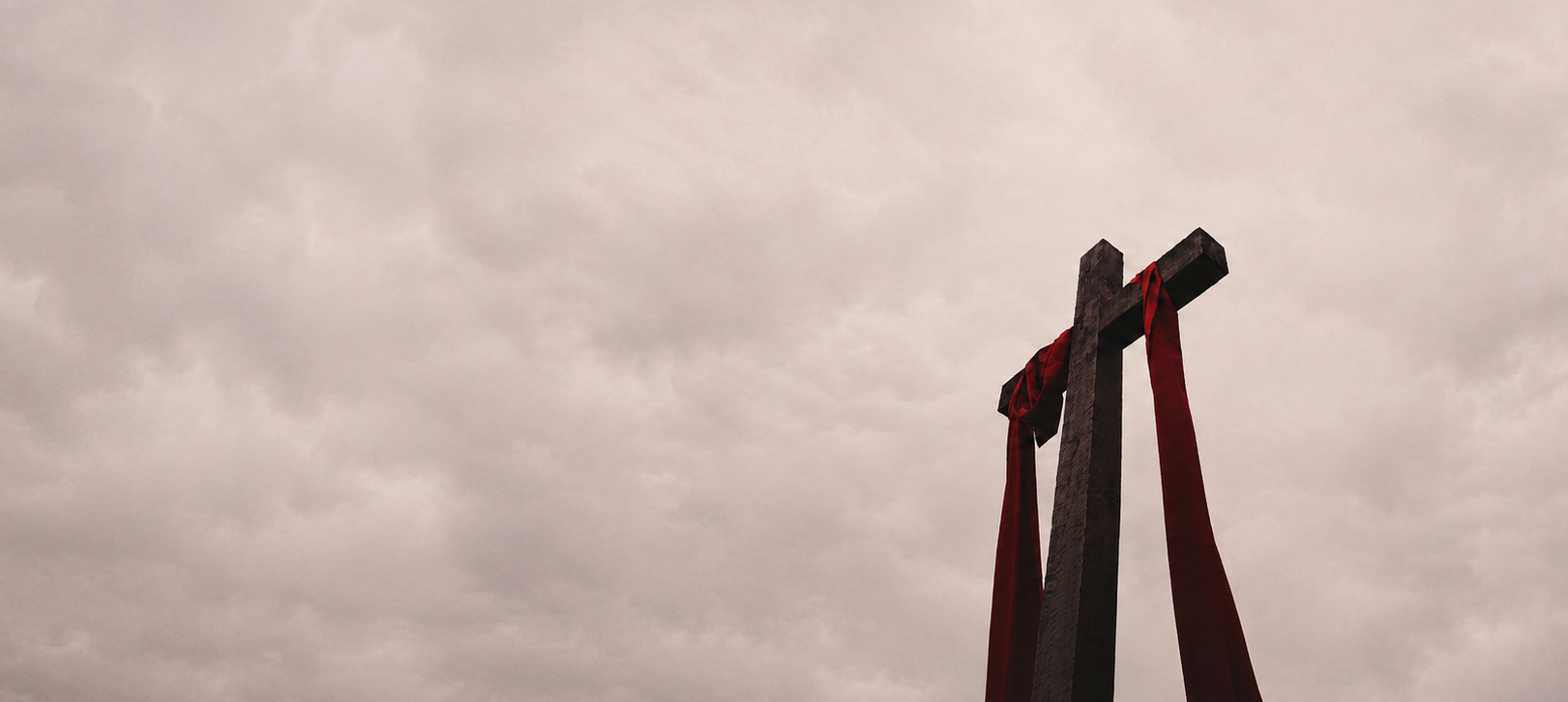 Wooden cross with red cloth against an overcast sky